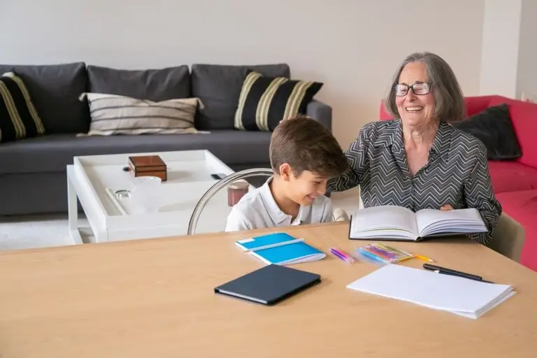 A grandmother laughs with her grandson at a table covered in notebooks and pens.